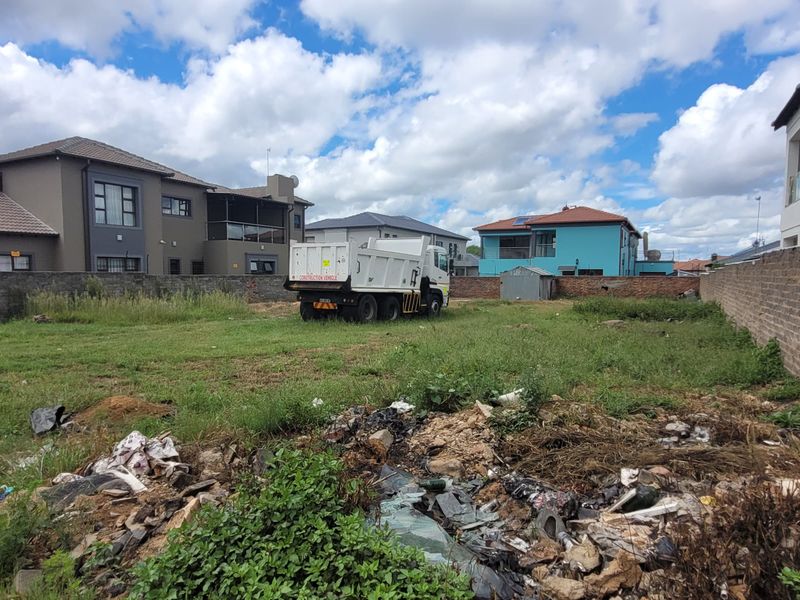 Vacant residential land plot enclosed by perimeter brick walls, currently featuring overgrown grass and accumulated debris.