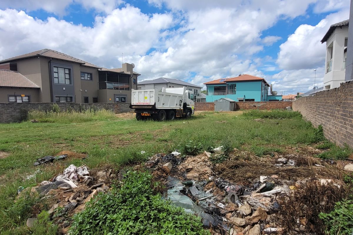A vacant residential plot enclosed by perimeter brick walls, currently featuring overgrown grass and accumulated debris on site.