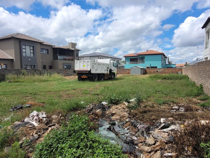 A vacant residential plot enclosed by perimeter brick walls, currently featuring overgrown grass and accumulated debris on site.