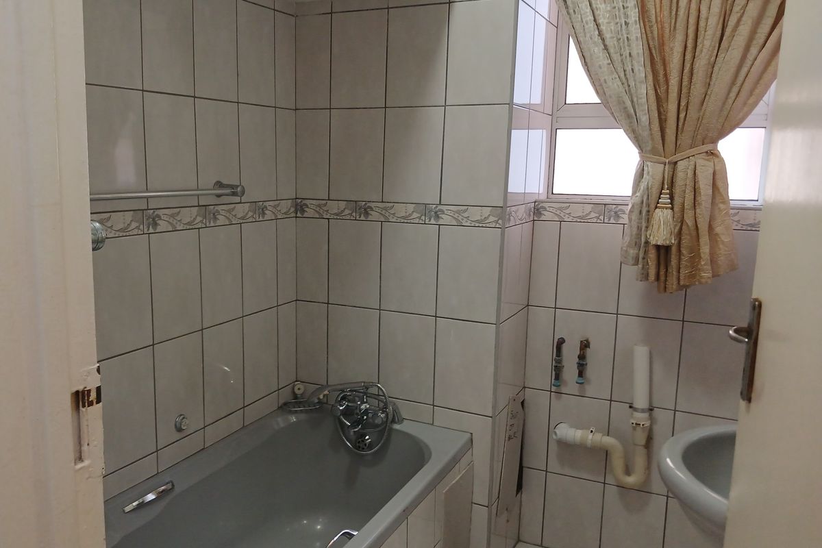 A functional bathroom featuring a bathtub and wall-to-floor tiling, currently requiring cosmetic updates and vanity installation to improve the overall aesthetic.