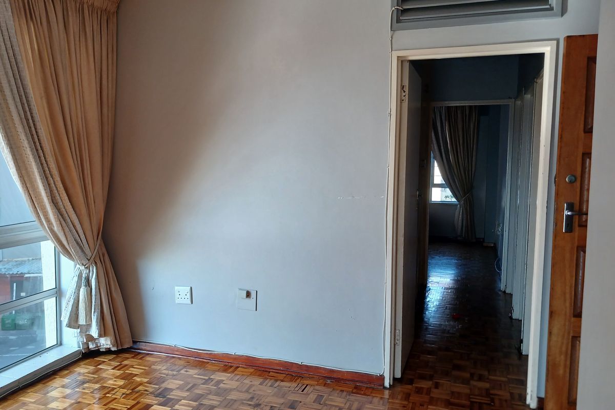 An empty bedroom featuring classic parquet flooring, neutral wall tones, and a doorway leading to a connecting hallway.