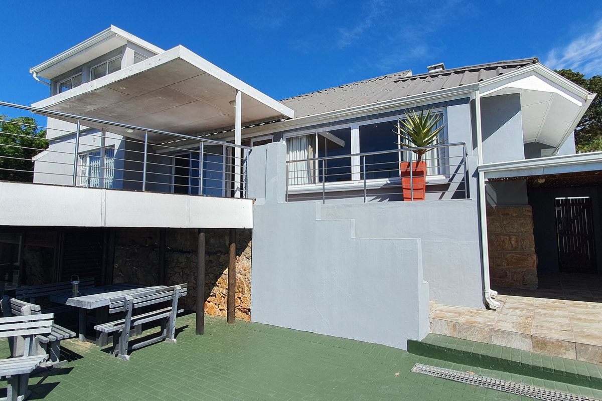 Rear exterior view featuring a raised deck with stainless steel balustrades, a tiled patio area, and a built-in braai, perfect for outdoor entertaining.