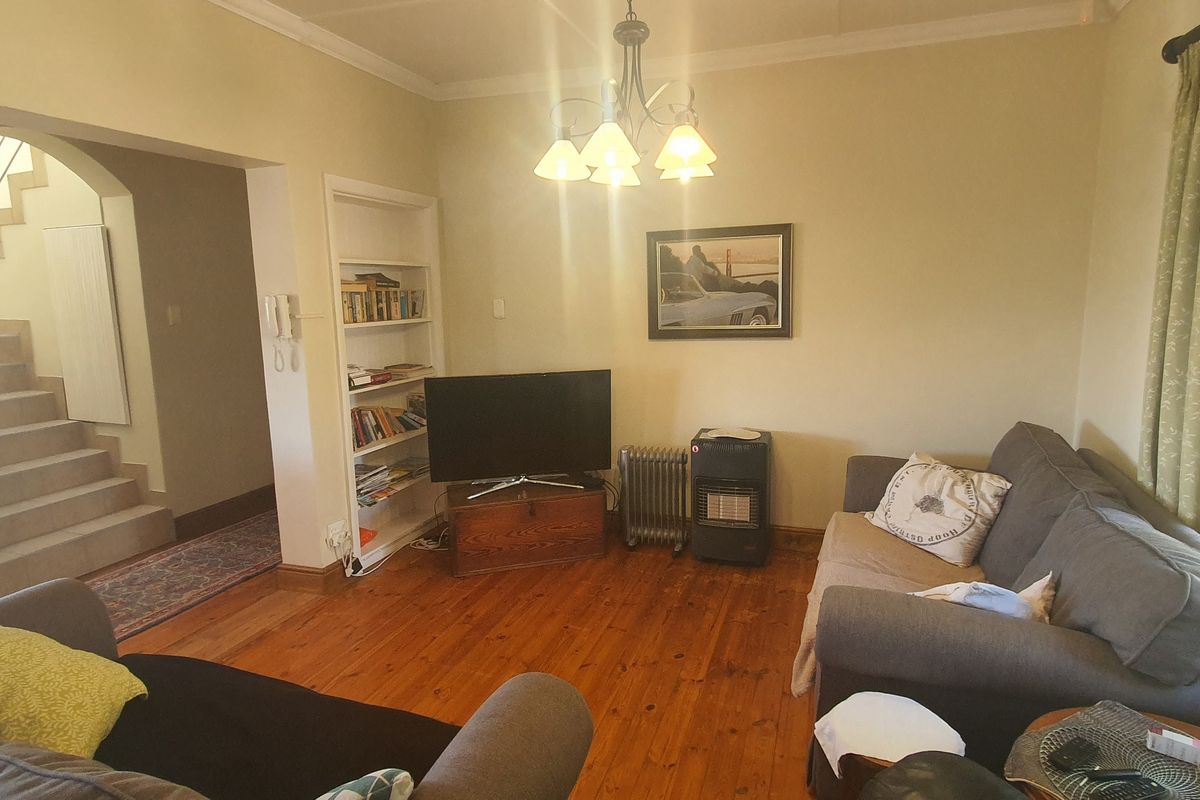 A living room featuring hardwood flooring, an arched entryway leading to a staircase, and built-in shelving.