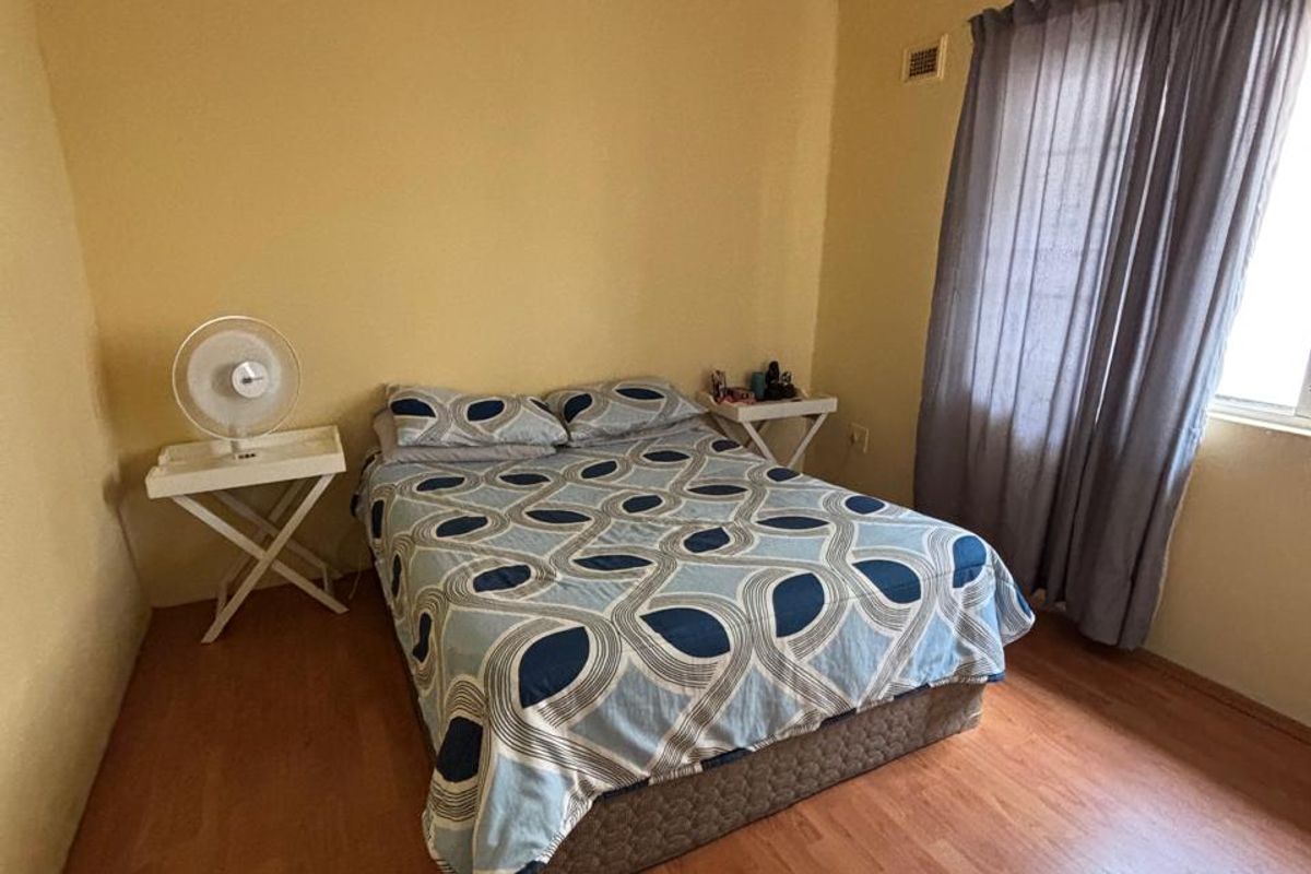 A bedroom featuring laminate flooring, a ceiling fan, and a window with curtains.
