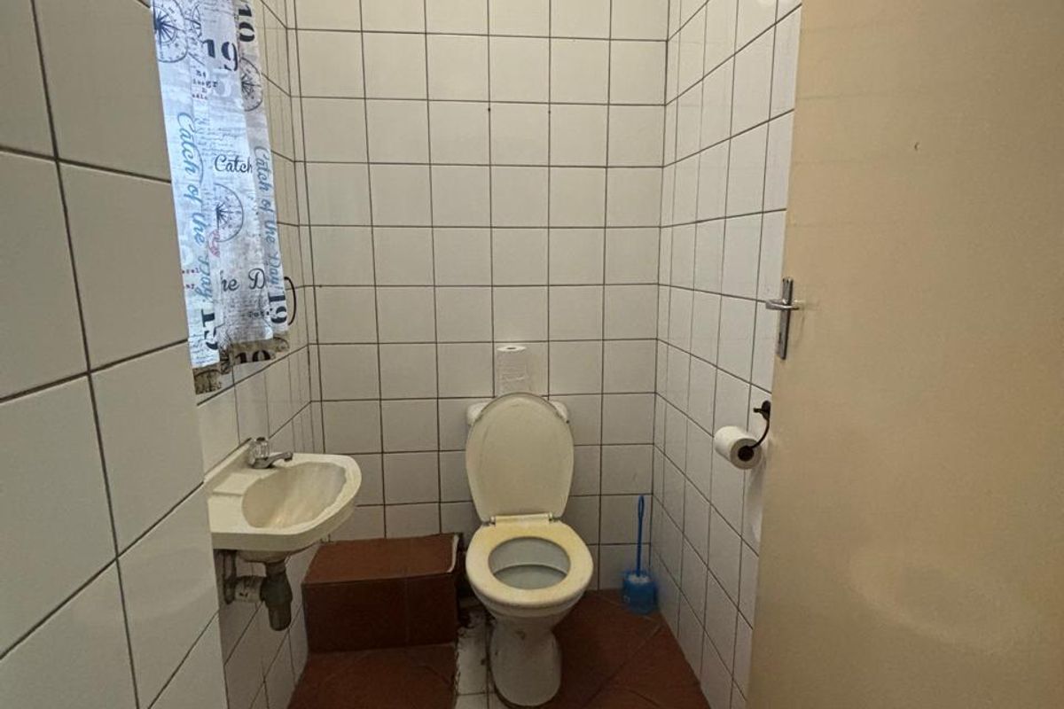 A compact guest bathroom featuring floor-to-ceiling white wall tiles, terracotta floor tiles, a wall-mounted basin, and a standard toilet.