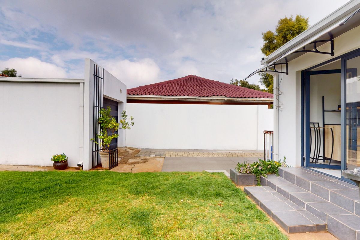 A view of the rear garden area featuring a paved patio, tiled steps leading to the house, and a detached garage structure.