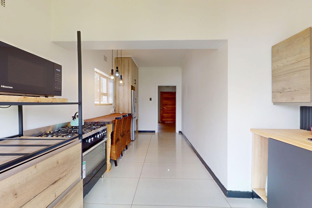 Modern kitchen featuring light wood cabinetry, a gas stove with extractor, and a breakfast bar, leading into an open-plan living area.