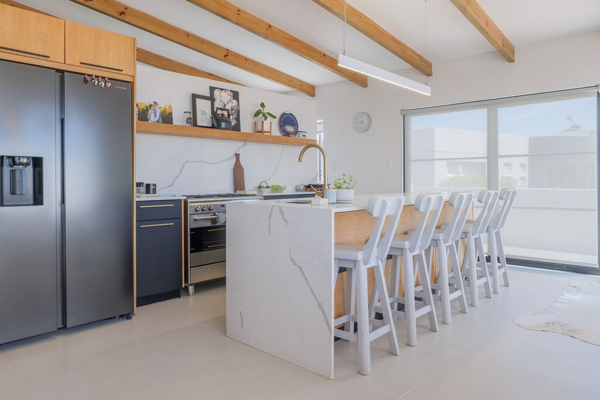 Modern kitchen featuring a large stone-topped island, exposed timber ceiling beams, high-end built-in appliances, and seamless access to an outdoor area.