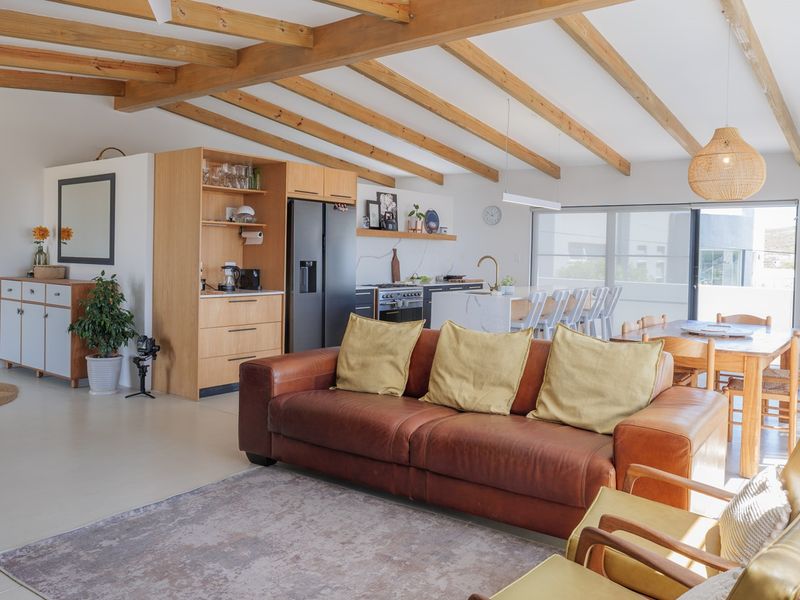Spacious open-plan living and kitchen area featuring exposed timber ceiling beams, modern cabinetry, a central island, and seamless access to outdoor space.