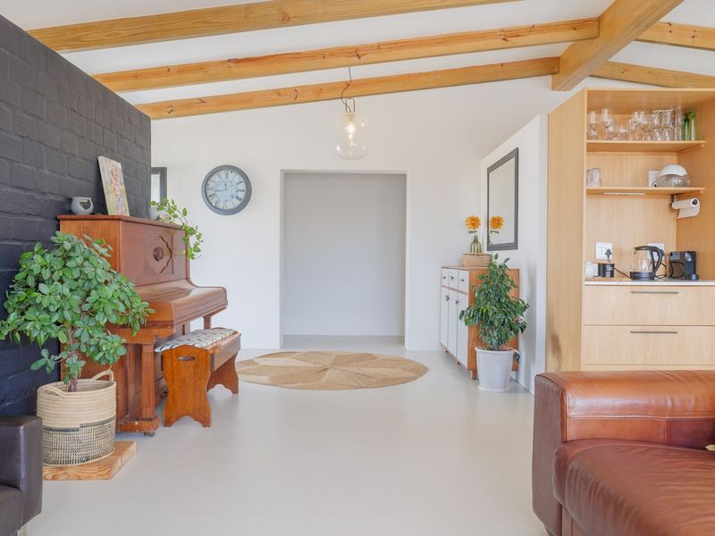 Open plan living area featuring exposed timber ceiling beams, a striking black painted brick feature wall, and modern polished concrete flooring.