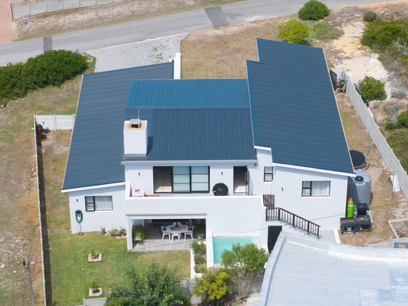 Aerial view of a residential property featuring a blue metal roof, swimming pool, covered patio, and an external staircase.