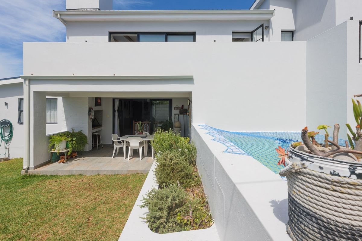 Rear view of the property featuring a covered patio with a built-in braai, adjacent swimming pool, and a landscaped garden area.