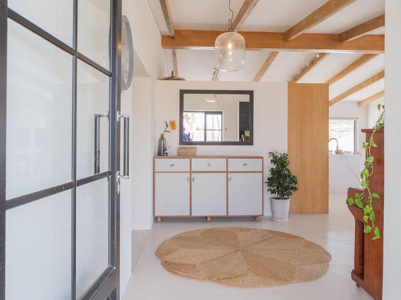 Bright and welcoming entrance hall featuring polished concrete floors, exposed timber ceiling beams, and a modern glass-panelled front door.