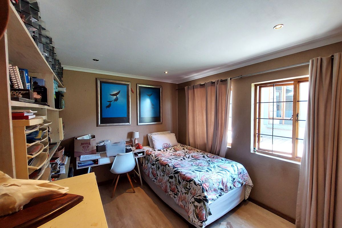 A functional bedroom featuring laminate flooring, recessed downlighting, and a built-in shelving unit, offering a comfortable space with natural light.