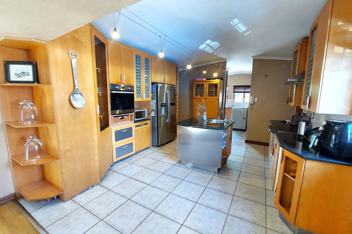 Spacious kitchen featuring extensive wooden cabinetry, granite countertops, a central stainless steel island, and built-in appliances with tiled flooring.