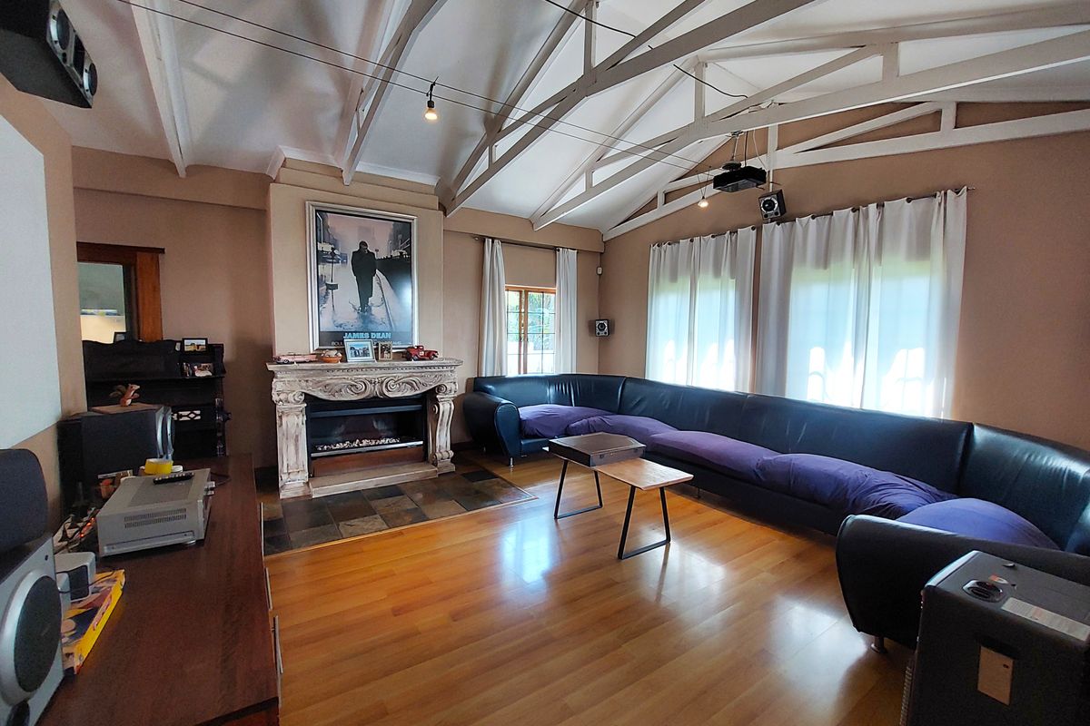 Spacious living room featuring a vaulted ceiling with exposed trusses, hardwood flooring, and a prominent fireplace with an ornate mantel.