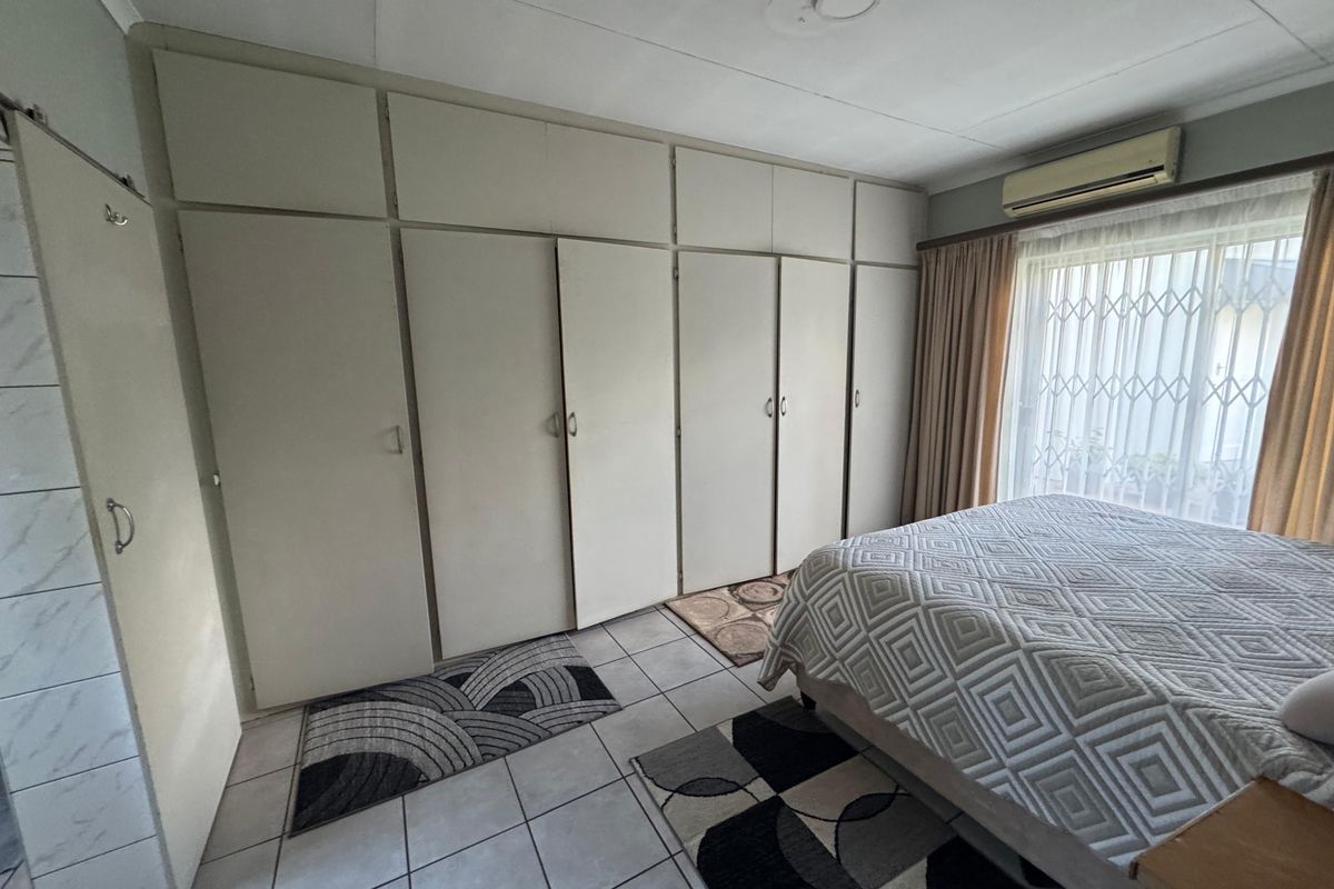 Bedroom featuring extensive built-in cupboards, tiled flooring, and a wall-mounted air conditioning unit with security gate access to the window.