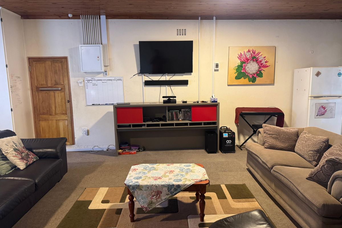 A living room featuring a timber ceiling and a solid wood door, with surface-mounted electrical infrastructure visible on the wall.