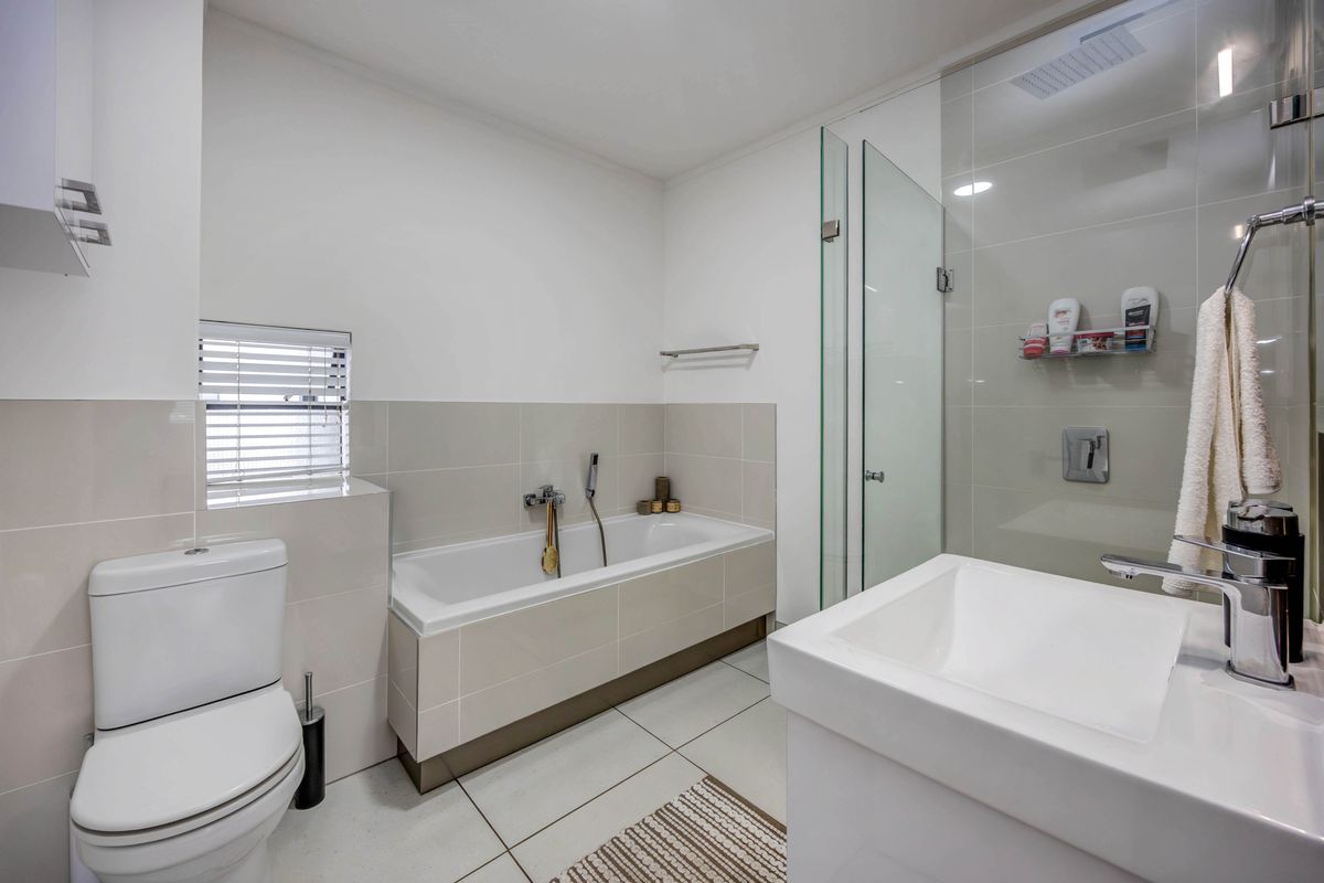 Modern bathroom featuring a built-in bathtub, separate glass-enclosed shower, vanity basin, and neutral tiled finishes throughout.