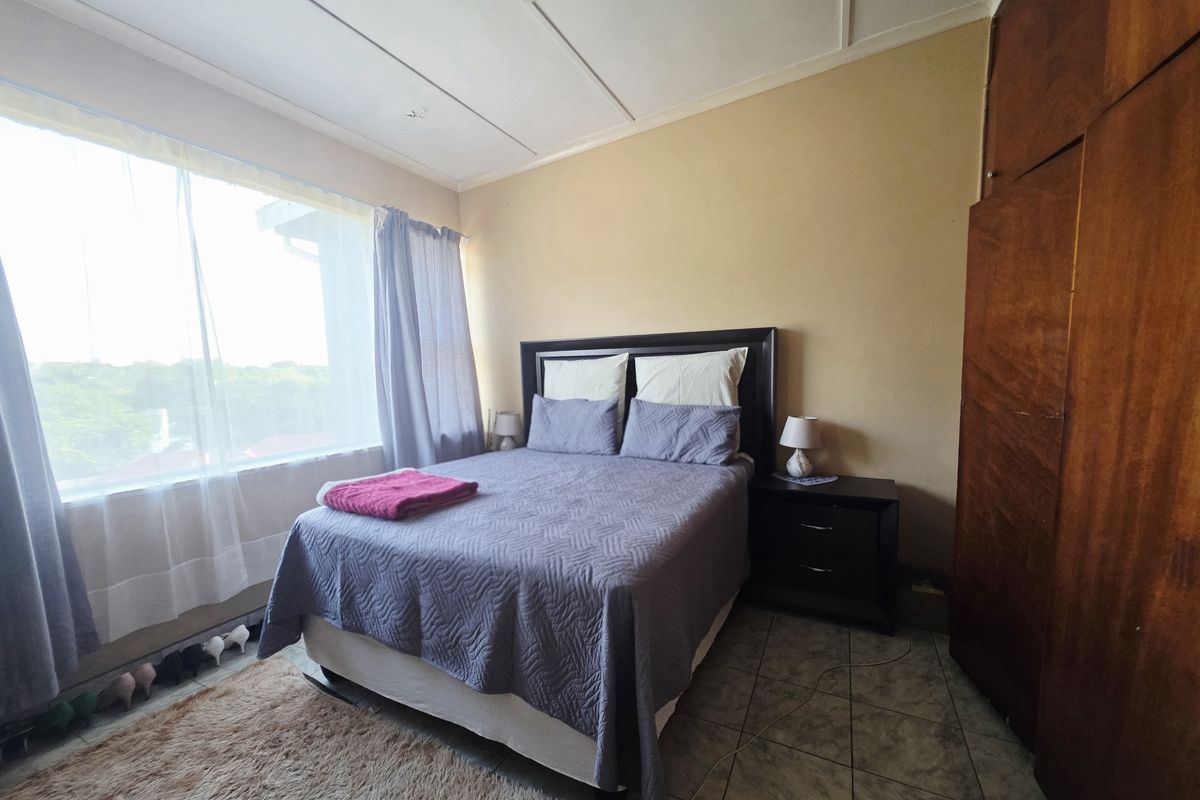 A bedroom featuring tiled flooring and a built-in wooden wardrobe, with large windows providing natural light.