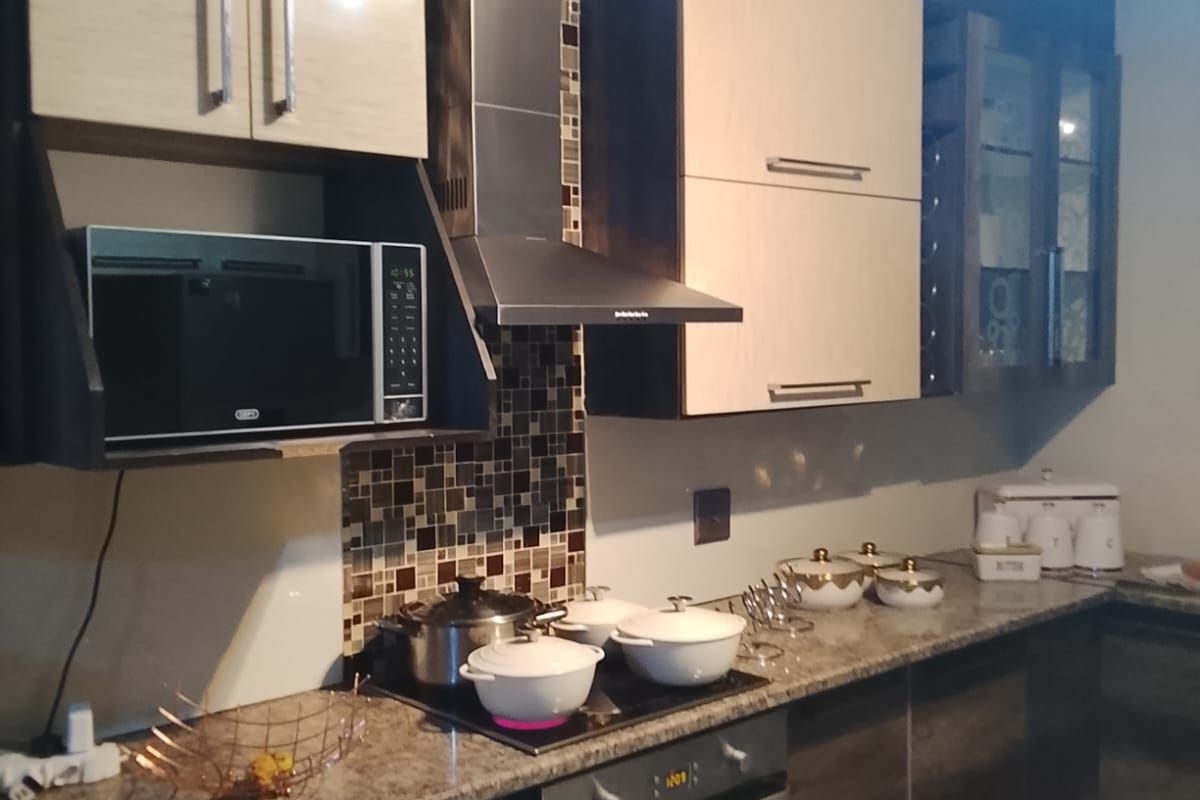 Modern kitchen featuring two-tone cabinetry, granite countertops, mosaic tile backsplash, built-in oven, glass hob, and stainless steel extractor fan.