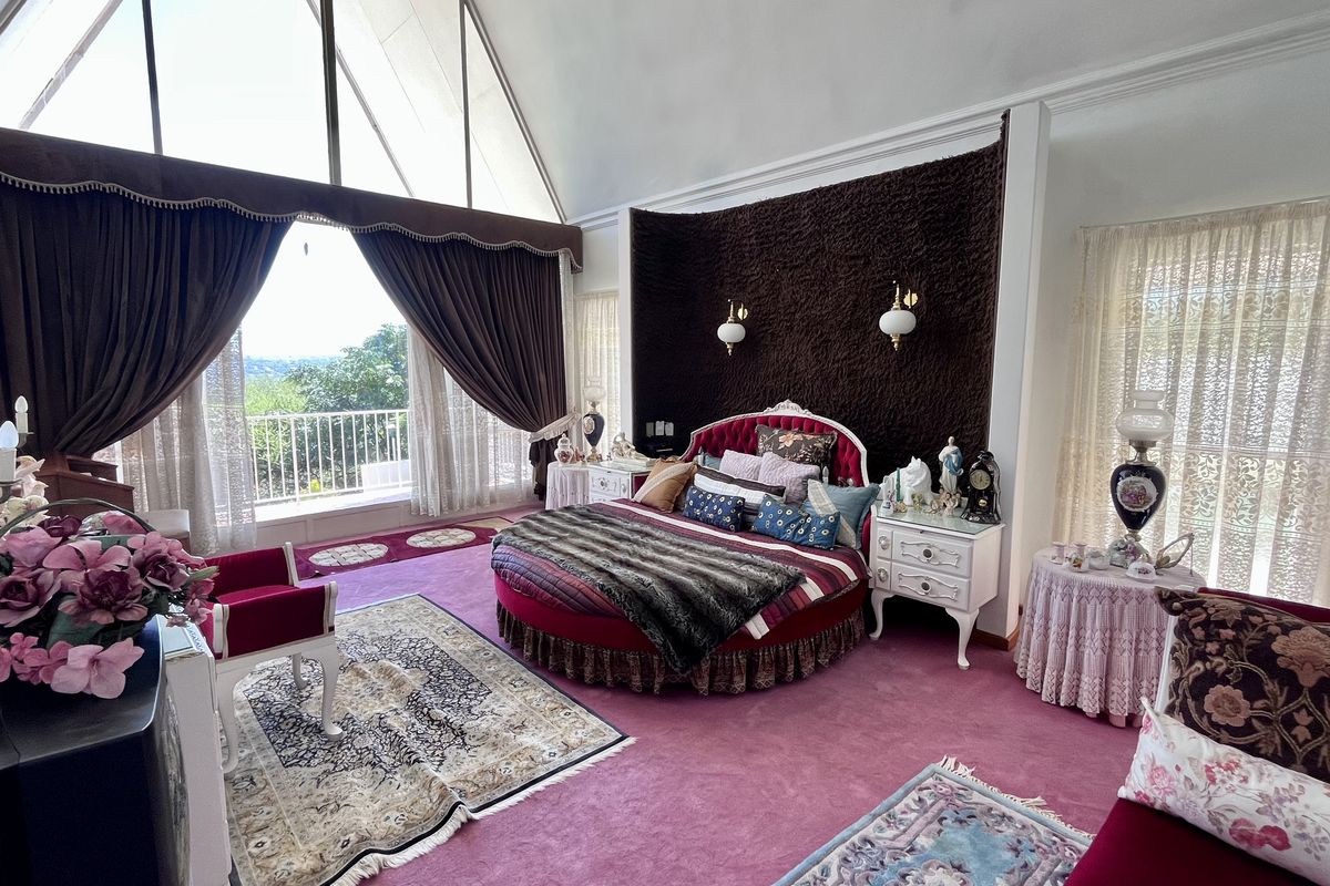 Spacious bedroom featuring a vaulted ceiling, large windows with balcony access, and unique architectural wall detailing.