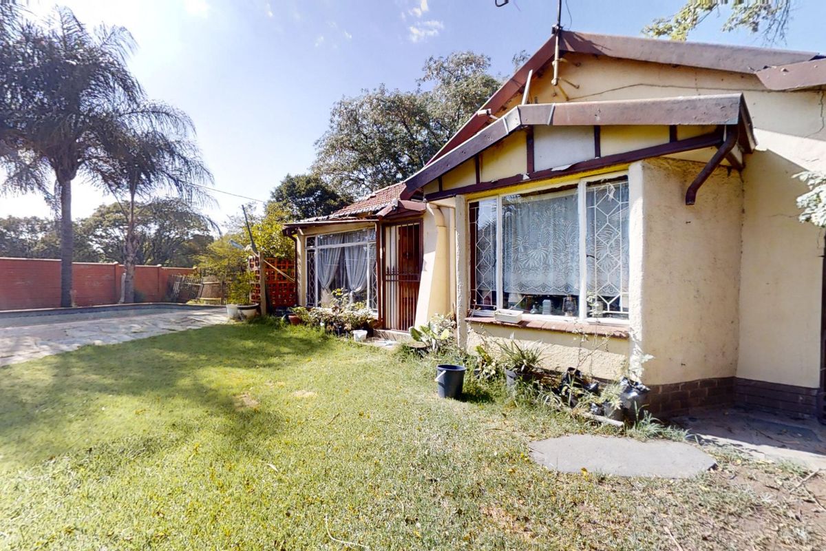 Rear view of the house featuring a paved patio, lawn, and brick boundary wall, showing signs of exterior wear and maintenance requirements.