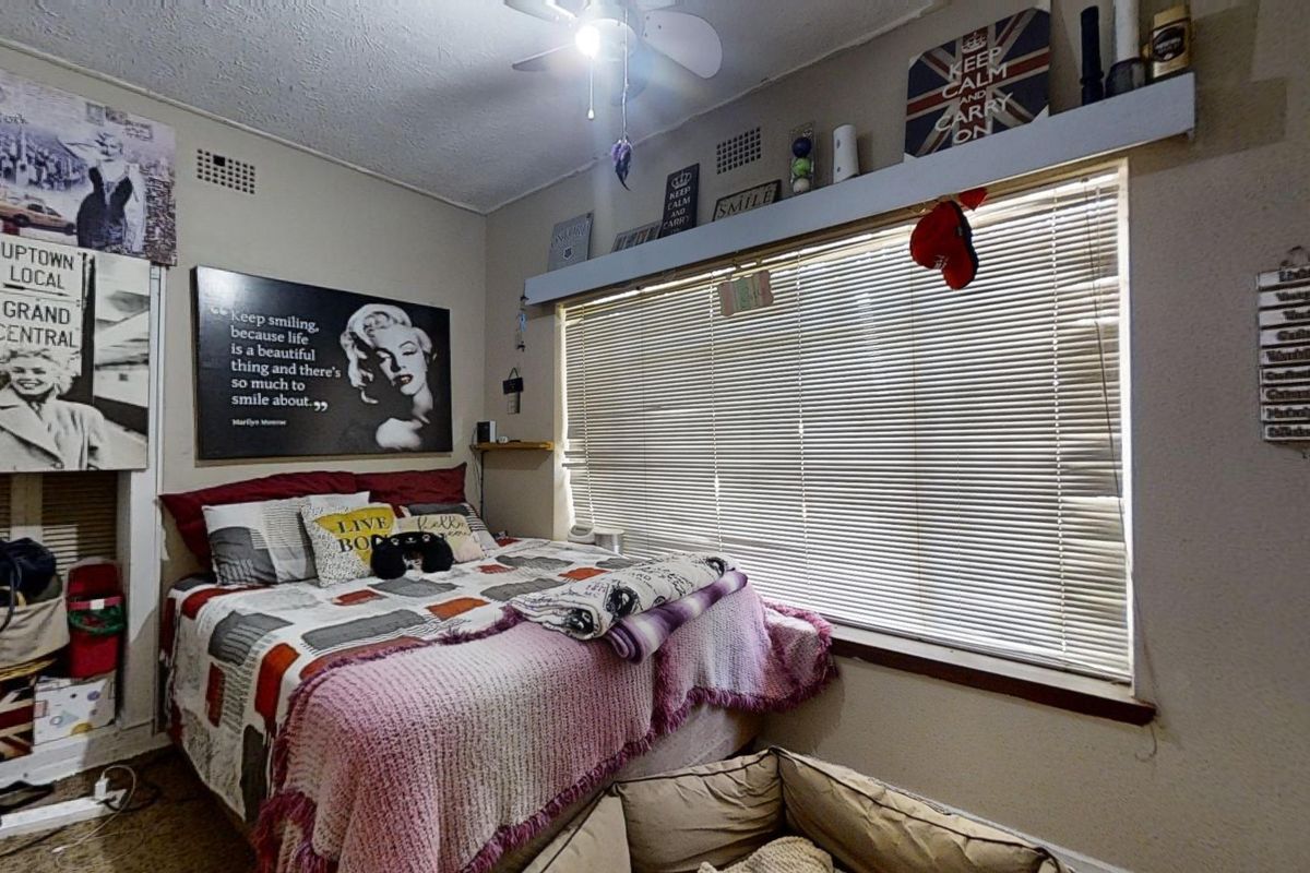 A bedroom featuring a ceiling fan, venetian blinds, and built-in shelving, providing a functional space with standard finishes.
