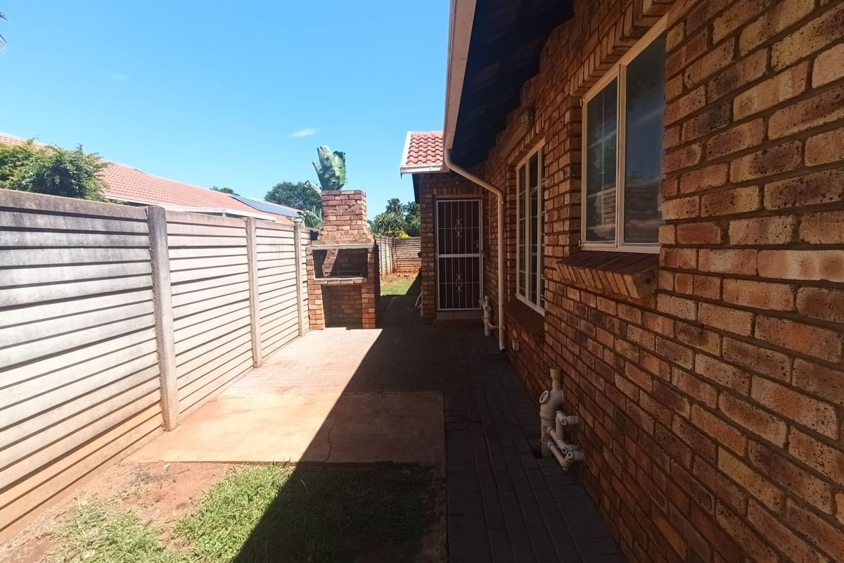 Rear exterior view featuring a brick facade, paved walkway, built-in brick braai, and precast concrete boundary wall in a retirement village setting.
