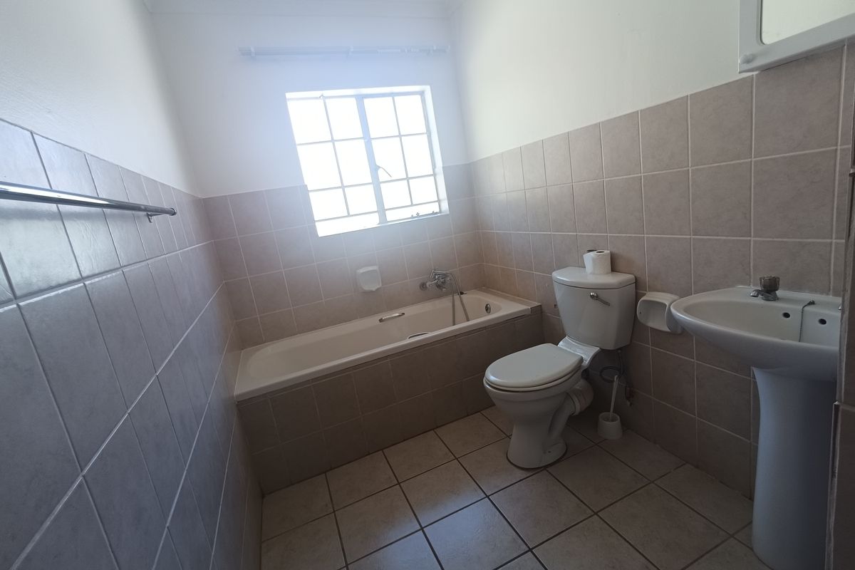 A functional bathroom featuring a bathtub, pedestal basin, and toilet with neutral ceramic wall and floor tiling.