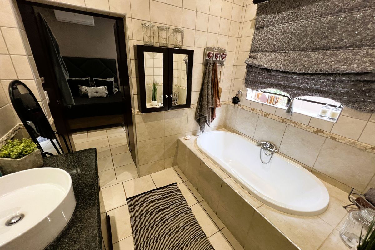 A bathroom featuring a built-in bathtub, tiled walls and flooring, and a vanity with a vessel sink, with direct access to the bedroom.
