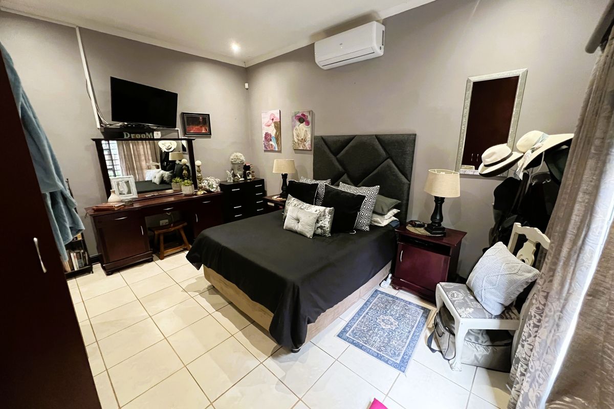 A well-proportioned bedroom featuring neutral wall tones, tiled flooring, and a wall-mounted air conditioning unit.