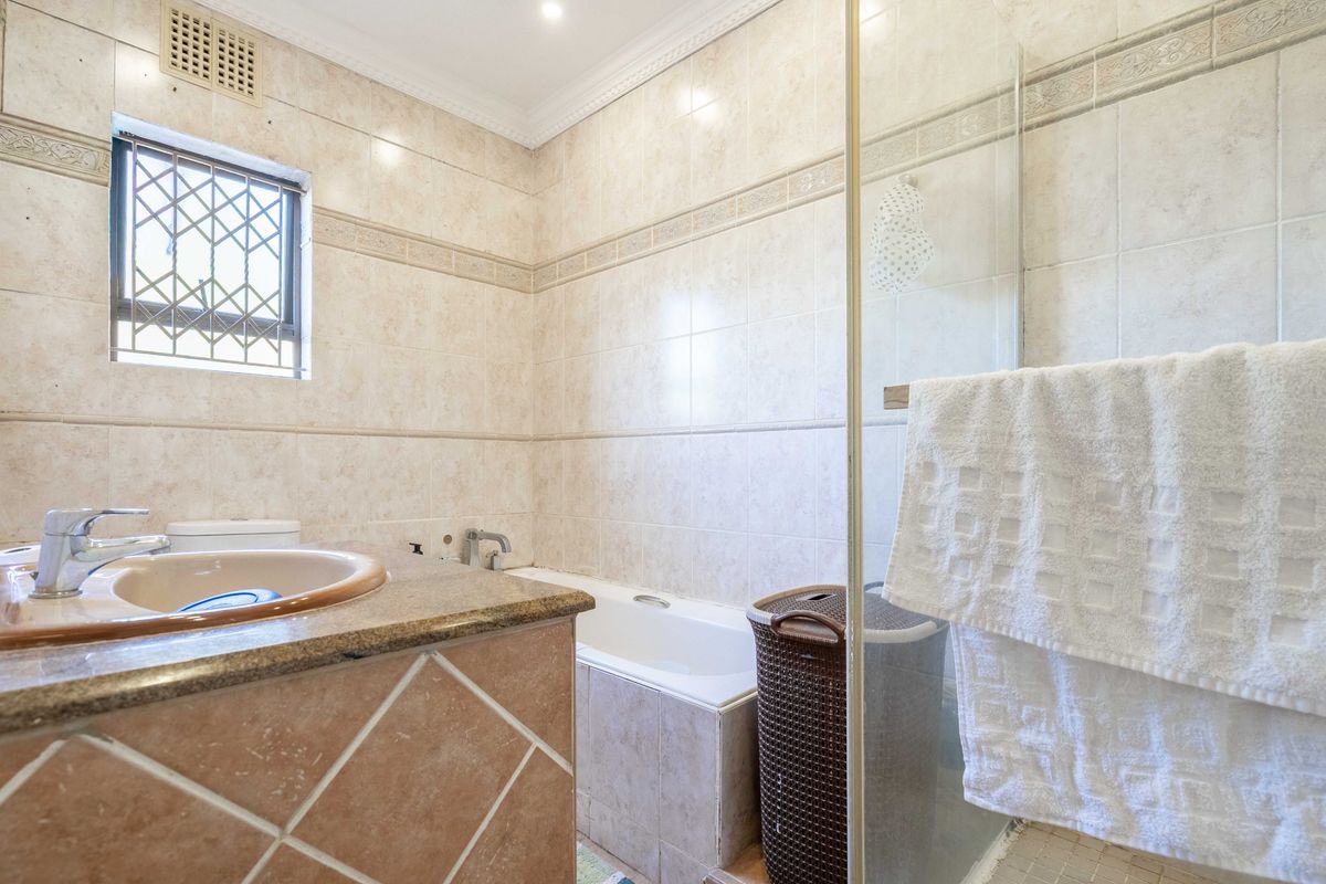 A functional bathroom featuring a built-in vanity with a stone countertop, a bathtub, and a separate glass-enclosed shower with neutral wall tiling.