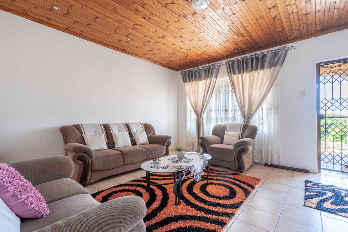A living room featuring a timber-clad ceiling, tiled flooring, and a security gate at the entrance.