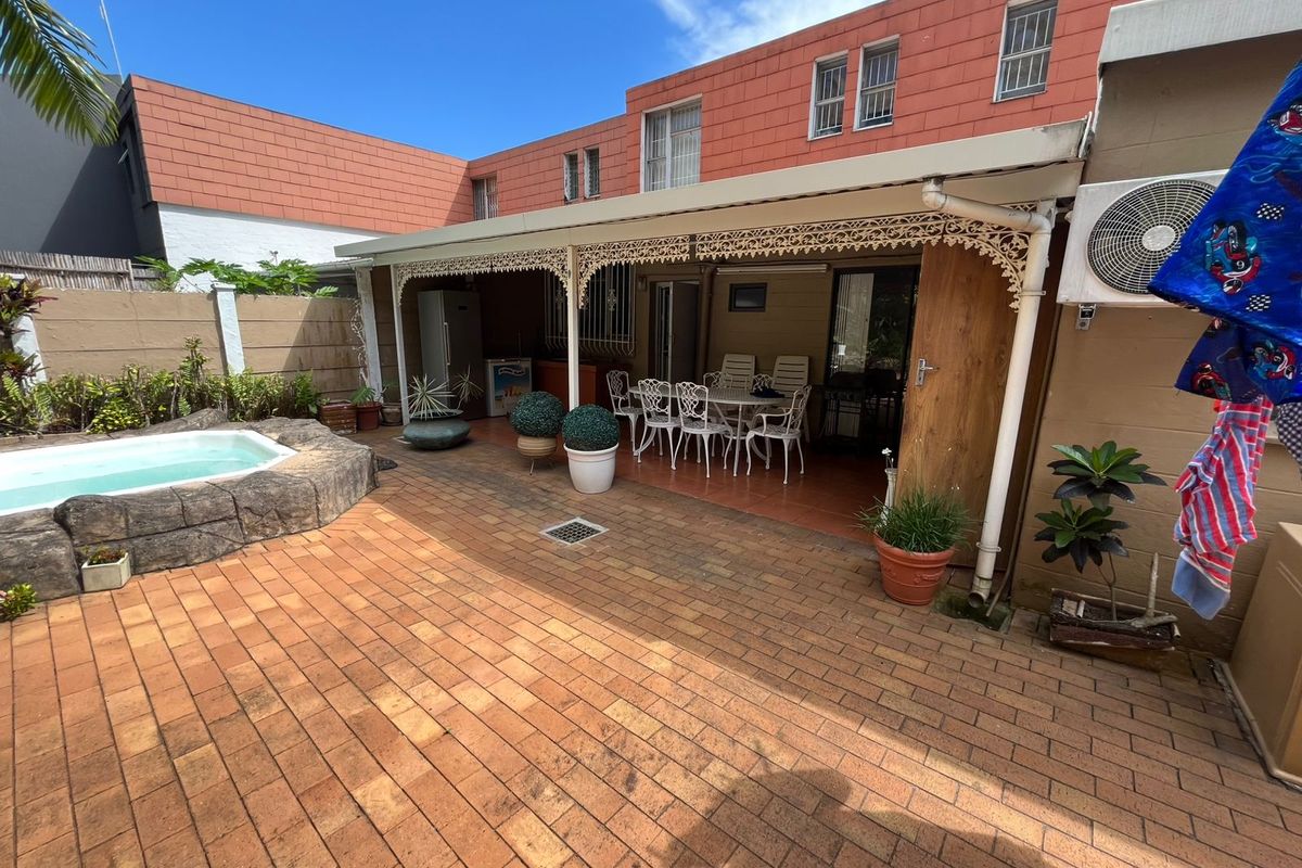 Rear exterior view featuring a covered patio area, brick paved courtyard, and a small swimming pool with rock-style surround.