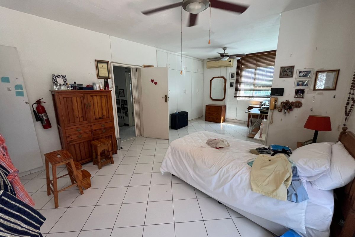 Spacious bedroom featuring tiled flooring, built-in cupboards, ceiling fan, and an air conditioning unit, requiring minor cosmetic updates to wall finishes.