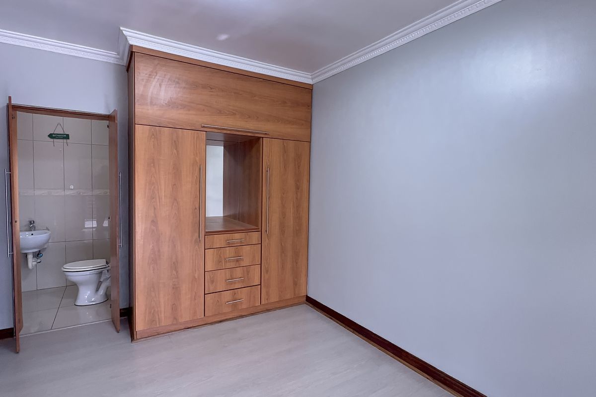 A spacious bedroom featuring built-in wooden cabinetry, crown molding, and direct access to an en-suite bathroom.