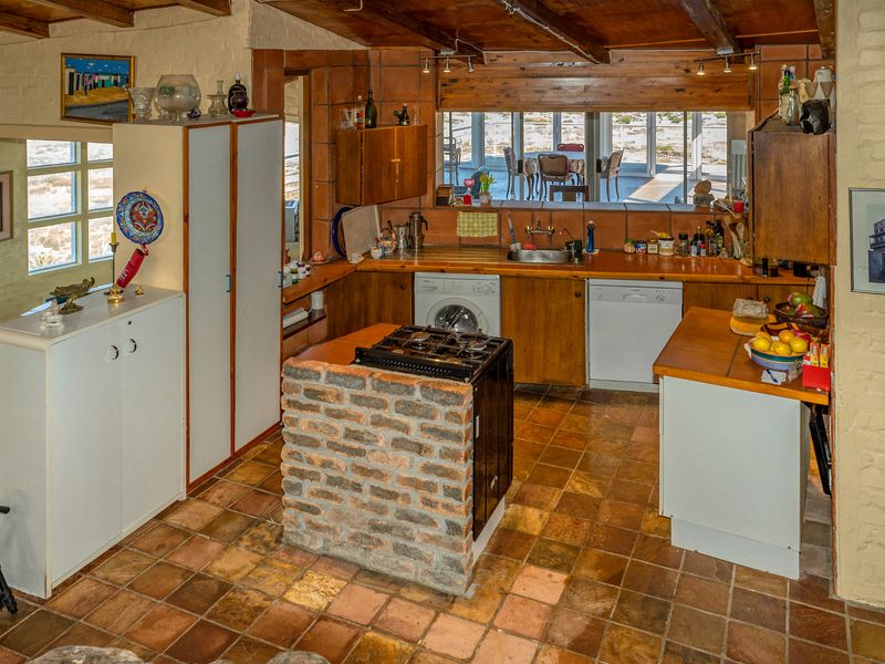 A rustic kitchen featuring exposed timber beams, a unique brick-encased gas hob island, tiled flooring, and built-in cabinetry with integrated appliances.