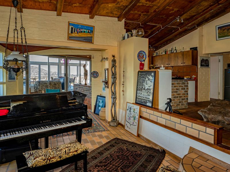 Spacious open-plan living area featuring exposed timber ceiling beams, tiled flooring, and a brick-accented kitchen, offering a rustic aesthetic with potential for modern updates.