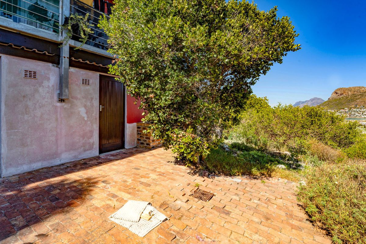 Rear exterior view featuring a brick-paved patio area, timber doors, and an elevated balcony overlooking the surrounding landscape.
