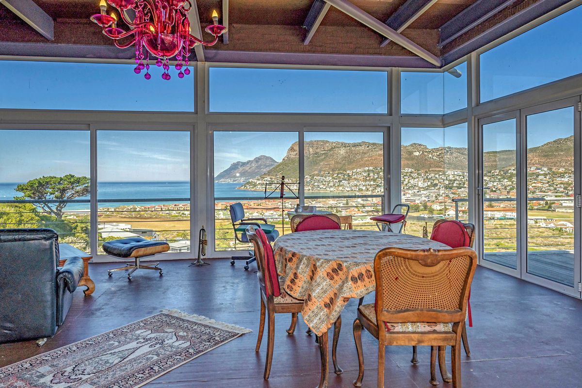 Spacious living area featuring expansive floor-to-ceiling windows and sliding doors that showcase panoramic coastal and mountain views, complemented by exposed timber ceiling beams.