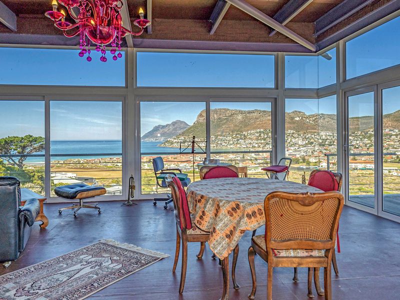 Spacious living area featuring expansive floor-to-ceiling windows and sliding doors that showcase panoramic coastal and mountain views, complemented by exposed timber ceiling beams.