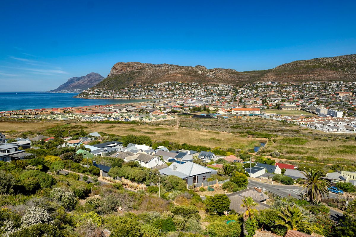 An elevated aerial view showcasing the coastal suburb, surrounding natural landscape, and mountain backdrop.