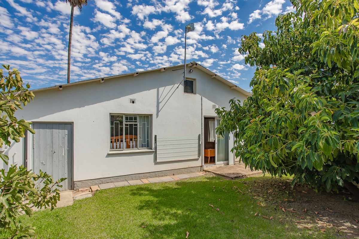 Rear view of the property featuring a white rendered facade, sliding glass door access, and a small concrete patio area overlooking the garden.