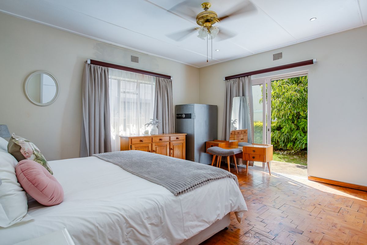 Spacious bedroom featuring classic parquet flooring, a ceiling fan, and direct access to the garden through a sliding glass door.