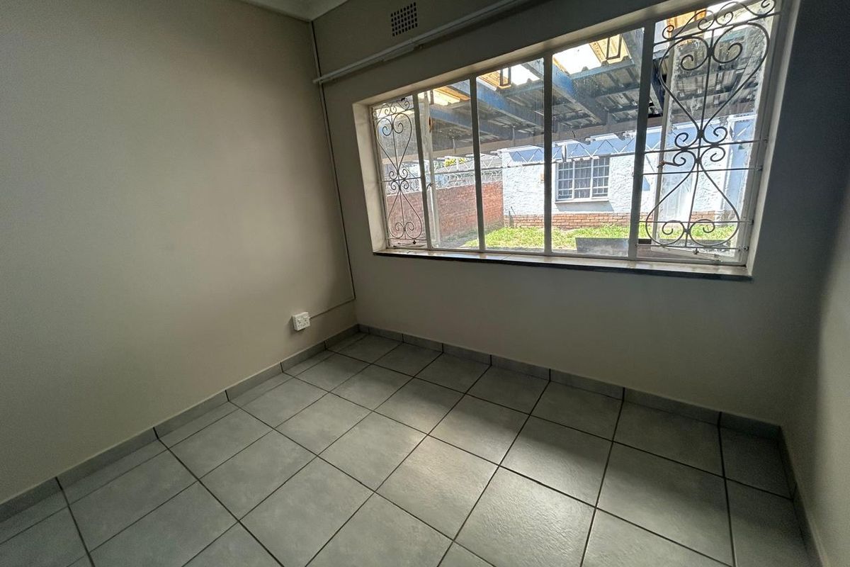 A vacant bedroom featuring neutral walls, tiled flooring, and a large window with security bars, offering a blank canvas for potential interior design.