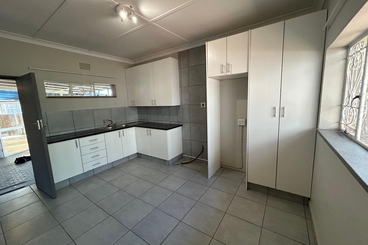 A clean, empty kitchen featuring white built-in cabinetry, dark countertops, tiled backsplash, and neutral floor tiles, offering a functional and well-maintained workspace.