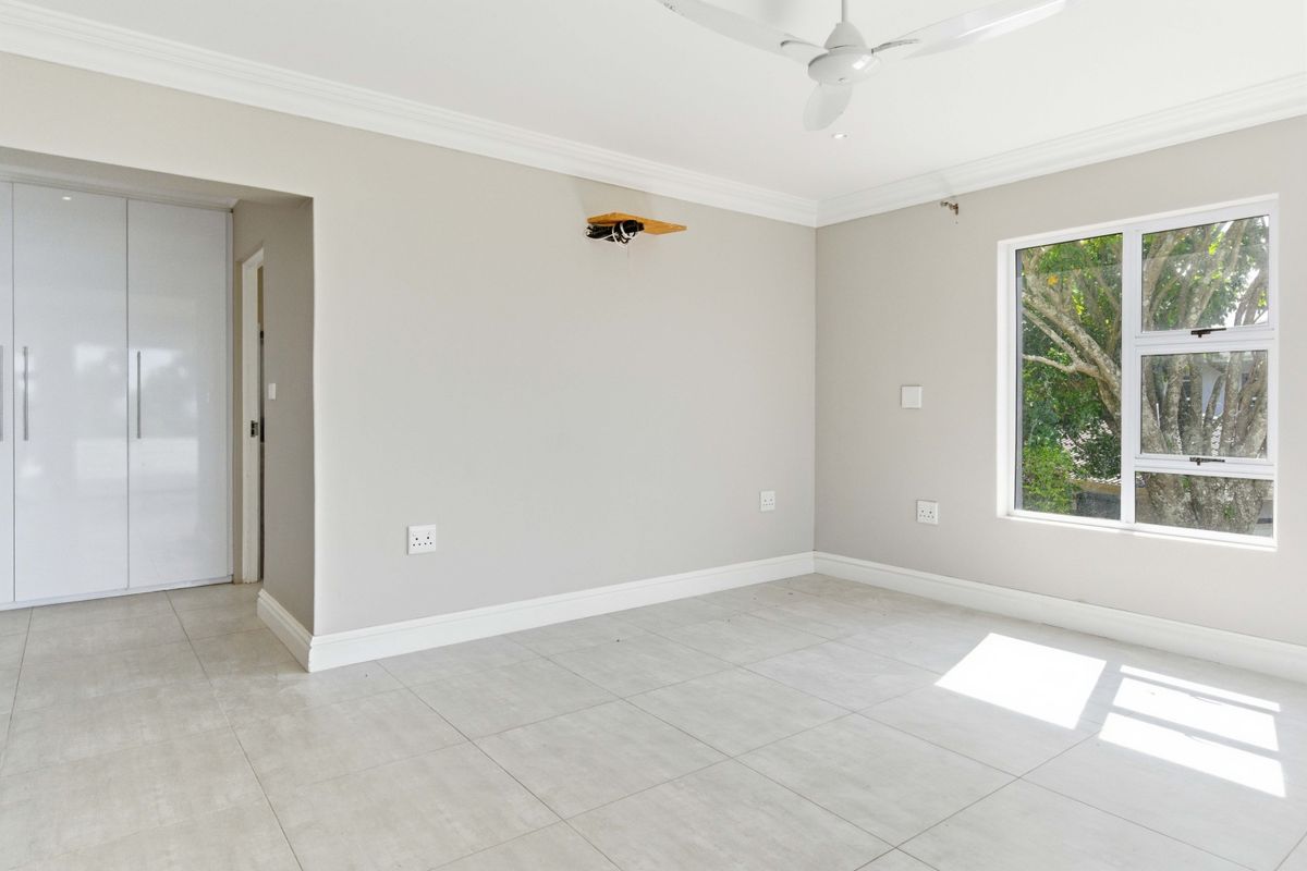 A bright, empty bedroom featuring neutral tiled flooring, built-in cupboards, and a ceiling fan, offering a clean and versatile living space.