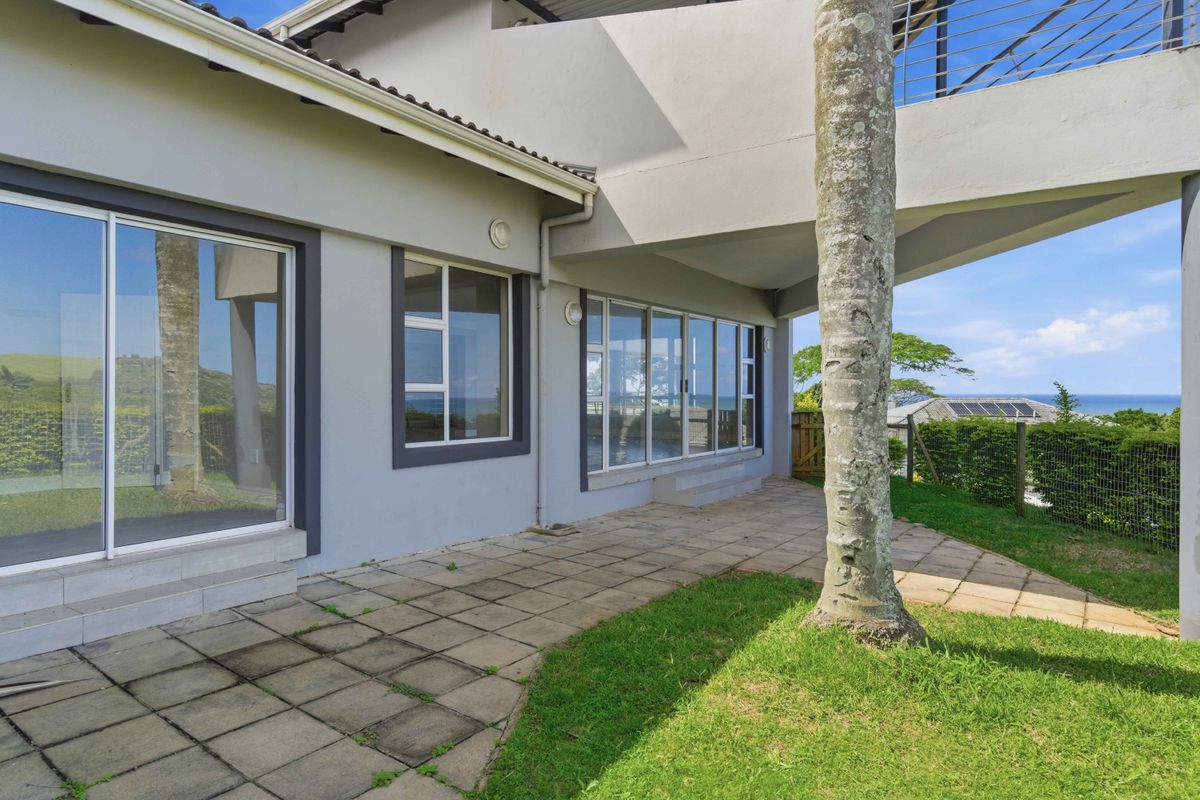 Rear exterior view of the townhouse featuring a paved patio area, sliding glass doors, and an elevated balcony overlooking the coastal landscape.