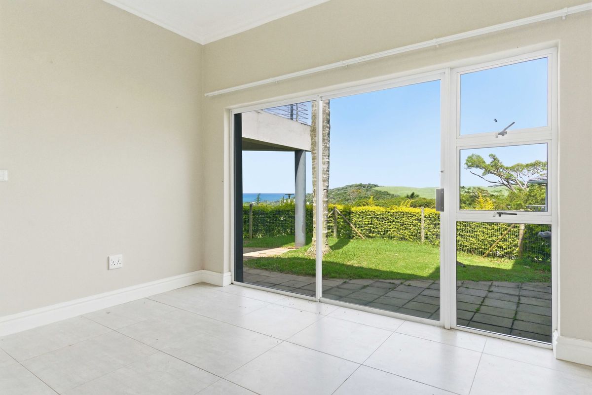 Bright and airy living space featuring large sliding glass doors that open onto a paved patio with scenic garden and coastal views.